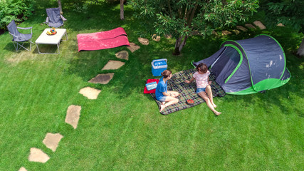 Aerial top view of campsite from above, mother and daughter having fun, tent and camping equipment...