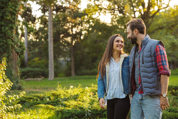 Fototapeta premium Image of caucasian couple man and woman looking at each other while walking together in green park