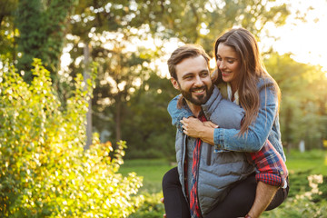 Image of masculine man giving piggyback ride to nice woman in green park