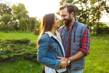 Fototapeta premium Image of pleased couple man and woman hugging and looking at each other while walking together in green park