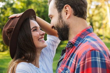 Image of joyful couple man and woman laughing while looking at each other in green park