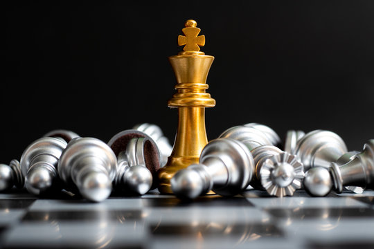 Gold king chess piece win over lying down silver pawn on black background