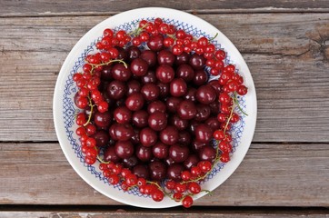Cherry and red currant in a plate and on a wooden table