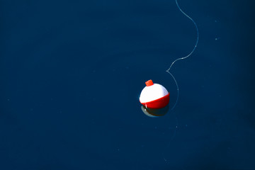 red and white floating fishing bobber with white fish line on dark blue water - obrazy, fototapety, plakaty