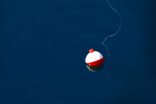 red and white floating fishing bobber with white fish line on dark blue water
