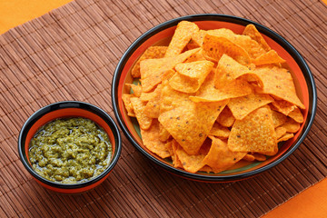 High angle view of basil pesto sauce with nachos corn chips in colorful plates on a bamboo table mat