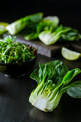 Baby bok choi halves, limes, green sprouts on black background