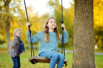 Cute young girl having fun on a swing in sunny autumn park. Family weekend in a city.