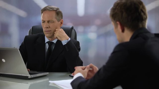Employer looking at laptop screen listening young candidate during job interview