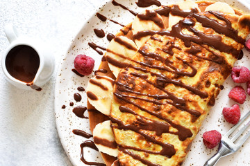 Crepe with chocolate paste, banana and raspberries on a concrete background. Tasty breakfast.