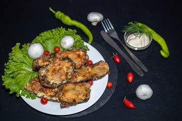 Eggplant stuffed with mushrooms and onions, rubbed with cheese, baked in the oven next to cherry tomatoes, lettuce. In the bowl sauce. All on a black background.