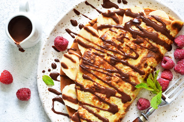 Crepe with chocolate paste, banana and raspberries on a concrete background. Tasty breakfast.