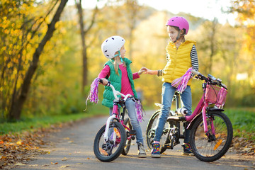 Cute little sisters riding bikes in a city park on sunny autumn day. Active family leisure with...
