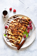 Crepe with chocolate paste, banana and raspberries on a concrete background. Tasty breakfast.