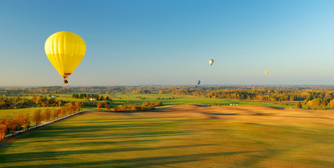 Colorful hot air balloon flying over forests surrounding Vilnius city on sunny autumn evening.