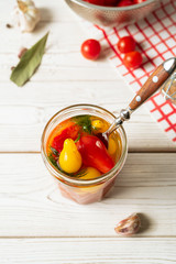 Marinated tomatoes in open glass jar, fork, cooking ingredients on white background. Horizontal image, top view.
