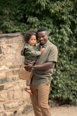 happy african american father holding his daughter on the hands standing on the street and looking at the camera