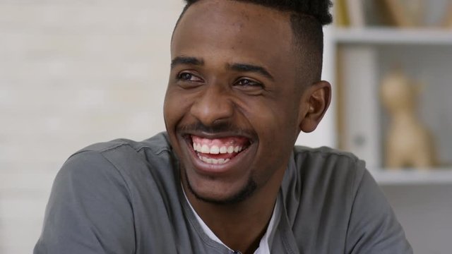 Tilting portrait shot of happy and carefree casually dressed young African American man talking to his coworkers at office and laughing