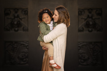 happy caucasian mother holding african american daughter on the hands
