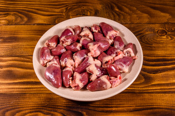 Ceramic plate with raw chicken hearts on wooden table