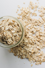 Jar and scatterd raw oat-flakes on white background