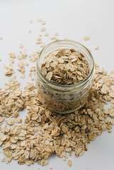 Jar and scatterd raw oat-flakes on white background