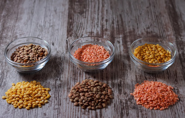 Green, red and yellow lentils in small glass bowls on wooden background. Indian kitchen