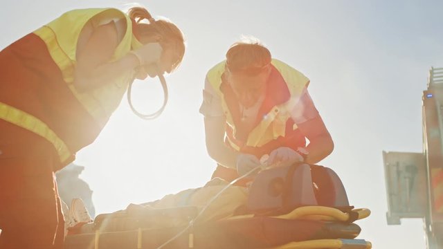 On the Car Crash Traffic Accident Scene: Paramedics Saving Life of a Traffic Accident Victim who is Lying on Stretchers. They Listen To a Heartbeat, Apply Oxygen Mask and Give First Aid Help