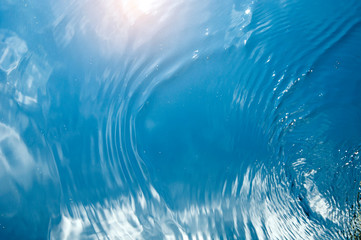 reflection of blue sky and sunlight on water surface with waves and bubbles blurred abstract background
