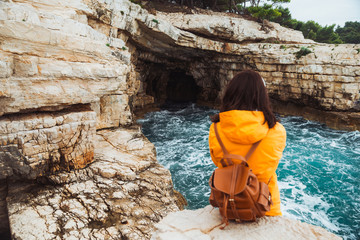Fototapeta premium young woman sitting at cliff looking at grotto cave with blue azure water