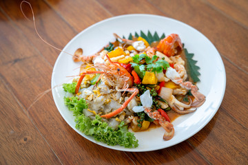 Seafood Thai mixxed together between boiled shrimp, crab, squid and colourful vegetable in dish on wood table in restaurant.