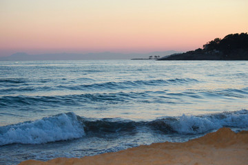 Landscape of tropical beach sunset. Waves, mountains, palm trees.