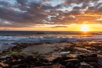 Dramatic sunset at the rocky beach with canoes in the background. Big Island Hawaii.