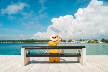 Naklejka na ściany i meble woman sitting on bench in yellow sundress enjoying the sea view