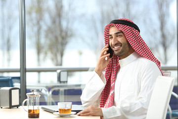 Happy arab man talking on phone in a coffee shop