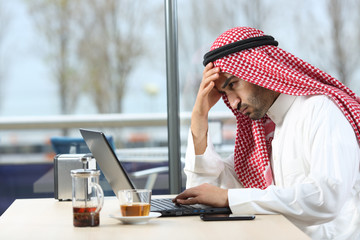 Confused arab man checking laptop in a bar