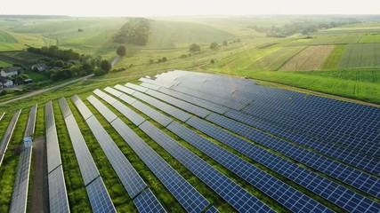 Flying over a solar farm with photovoltaic panels converting solar power to electricity for green energy on agricultural land - Powered by Adobe