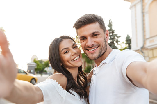 Portrait closeup of brunette young couple smiling and taking selfie photo while walking outdoors