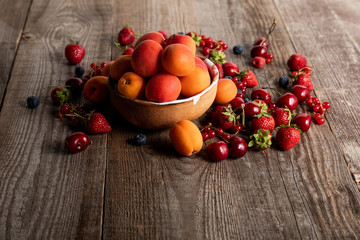 ripe delicious seasonal berries scattered around bowl with apricots on wooden table
