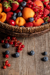 Fototapeta na wymiar close up view of ripe berries and apricots in wicker basket on wooden table