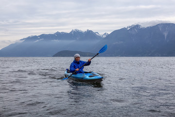 Adventurous man on a kayak is paddling in Howe Sound during a cloudy evening. Taken near Bowen Island, Northwest of Vancouver, BC, Canada.