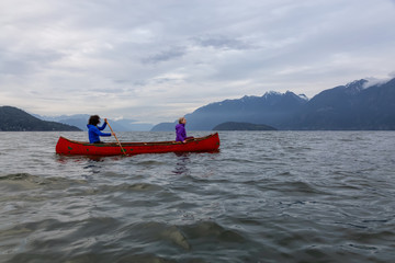 Couple adventurous female friends on a red canoe are paddling in the Howe Sound during a cloudy...
