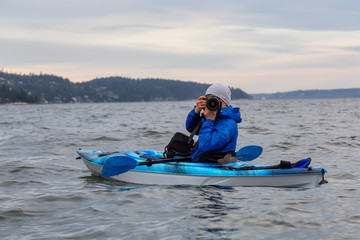 Naklejka premium Adventure photographer taking pictures with his camera from a kayak in the ocean. Taken in Howe Sound near Horseshoe Bay, West Vancouver, British Columbia, Canada.