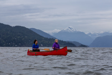 Couple adventurous female friends on a red canoe are paddling in the Howe Sound during a cloudy...