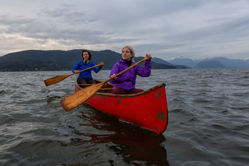 Couple adventurous female friends on a red canoe are paddling in the Howe Sound during a cloudy...