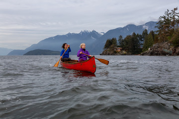 Couple adventurous female friends on a red canoe are paddling in the Howe Sound during a cloudy...