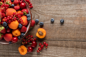 Fototapeta na wymiar top view of ripe fresh berries and apricots on plate on wooden table
