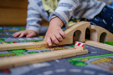 baby hands playing with wooden train set on wooden rails on a carpet in nursery