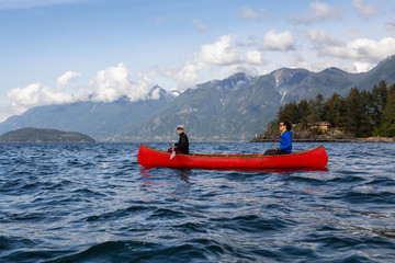 Couple adventurous female friends on a red canoe are paddling in the Howe Sound during a cloudy and...