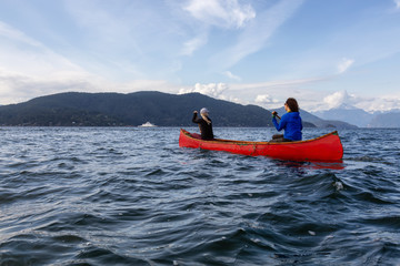 Couple adventurous female friends on a red canoe are paddling in the Howe Sound during a cloudy and sunny evening. Taken near Horseshoe Bay, West of Vancouver, BC, Canada.